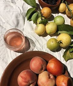 a bowl of peaches and some lemons on a white table cloth next to a glass of water