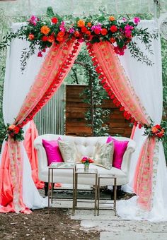 a white couch with pink and red flowers on it under an outdoor wedding ceremony canopy