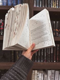 a person holding an open book in front of a bookshelf full of books