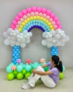 a woman sitting on the ground in front of balloons and a rainbow arch with flowers