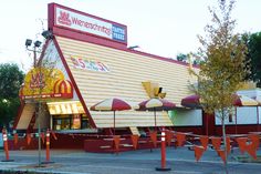 an outside view of a restaurant with red and white striped awnings, yellow umbrellas and trees