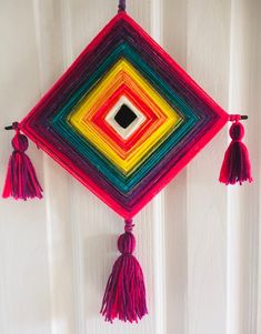 a multicolored wall hanging with tassels on the sides and a black square in the center