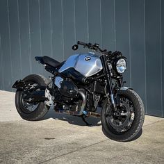 a silver and black motorcycle parked in front of a gray wall on the side of a road