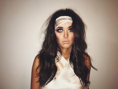 a woman with long hair and bandages on her head is posing in front of a white wall