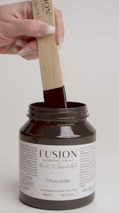 a person holding a wooden stick over a jar filled with chocolate paste and fuson