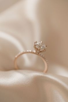 an engagement ring sitting on top of a white satin cloth with a diamond in the center