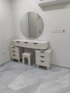 a white vanity with drawers and a round mirror on the wall in a corner room