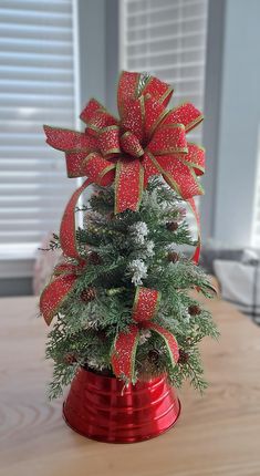 a small christmas tree in a red pot with bows on it's top, sitting on a table