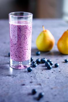 a glass filled with blueberries next to two pears