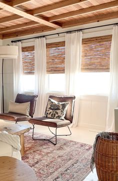 a living room filled with furniture and windows covered in shades of white drapes on top of them