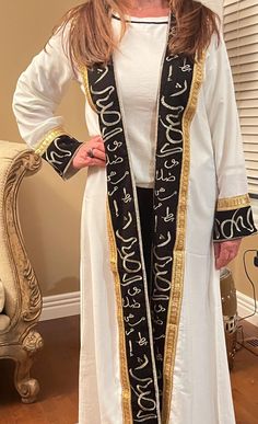 Open long Arabic calligraphy white and black kaftan. Gold embroidery. Free size. Cotton. White Kaftan With Gold Embroidery For Eid, White Long Sleeve Kaftan With Gold Embroidery, White Gold Embroidered Kaftan For Eid, Traditional Long White Abaya, Elegant White Kimono For Eid, Embroidered White Tunic Thobe, White Embroidered Long Thobe, White Embroidered Long Sleeve Thobe, Traditional White Tunic Abaya