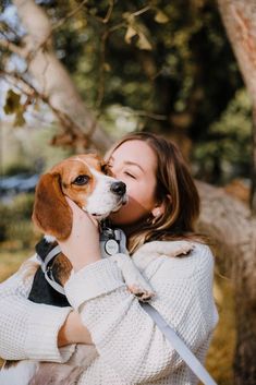 a woman holding a dog in her arms and kissing it's face while standing under a tree