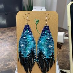 a pair of blue and black beaded earrings sitting on top of a wooden stand