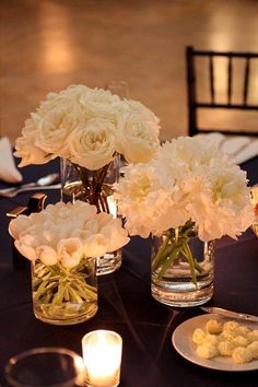 white flowers are in vases on a table with candles and place settings for dinner