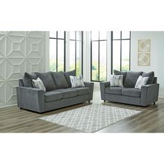 two gray couches sitting next to each other on top of a wooden floor in front of large windows