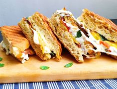 two sandwiches cut in half sitting on top of a wooden cutting board next to green leaves