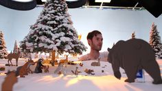 a man standing in front of a fake christmas tree with animals around it and snow on the ground