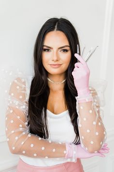 a woman wearing pink gloves and holding scissors in one hand while standing against a white wall