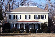 a large white house with black shutters on the front and side windows, surrounded by trees