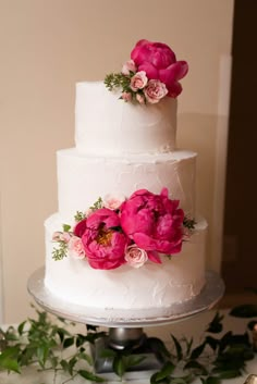 a three tiered white cake with pink flowers on top and greenery around it