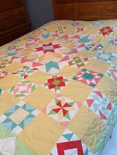 a bed with a colorful quilt on it's headboard and dressers in the background