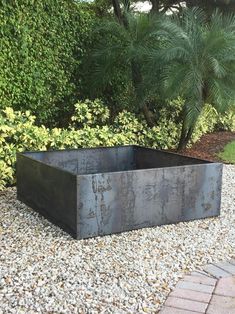 a large metal planter sitting on top of a gravel covered ground next to trees