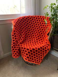 an orange knitted chair next to a potted plant