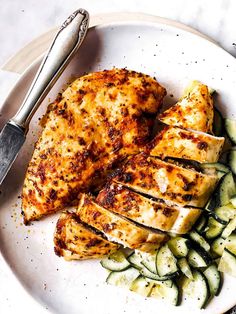 grilled chicken and cucumbers on a white plate with a silver serving utensil