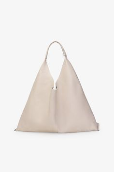 Marcella’s Kelly Tote is an oversized white handbag made of genuine Italian leather featuring a triangular silhouette with a wide opening and a magnetic closure. Triangle Tote, Cole Buxton, Leather Work Bag, Silver Handbag, Structured Shoulder, Oversized Tote Bag, Build A Wardrobe, Shoulder Sling, Oversized Tote