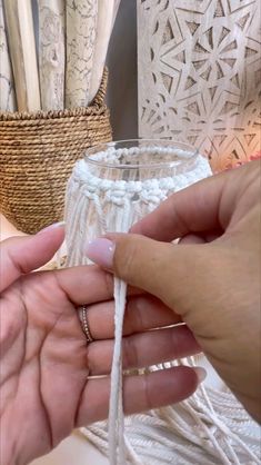 a person is holding yarn in their hand and weaving it into a glass vase with white crochet