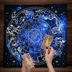 two hands holding cards in front of a zodiac sign on a blue background with stars