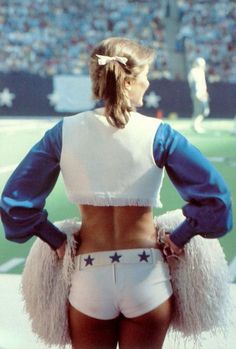 a cheerleader is standing on the sidelines at a football game with her back to the camera