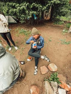 a woman sitting on the ground next to some rocks and trees with her legs crossed