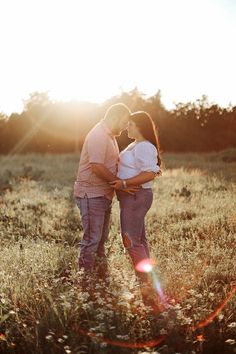 a man and woman standing in a field with the sun shining through the trees behind them