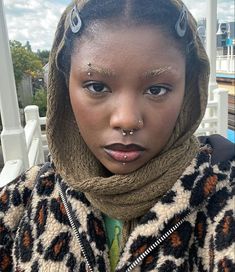 a woman with piercings on her nose wearing a leopard print jacket and scarf over her head