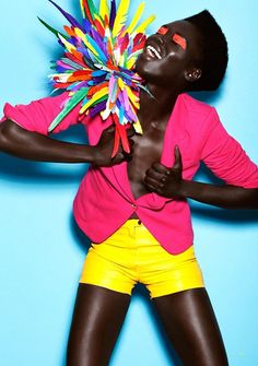 a woman in yellow shorts and pink shirt holding a multicolored object up to her face