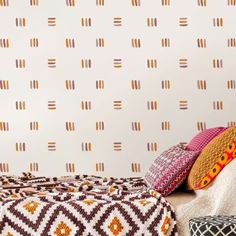 a bed with colorful pillows on top of it next to a wallpapered headboard