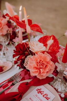 the table is set with red and pink flowers, silverware, and napkins