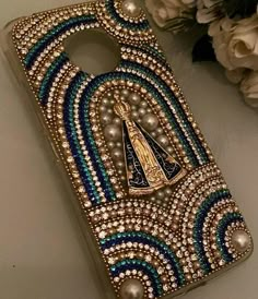 a cell phone case with pearls and other beads on it, sitting next to some flowers