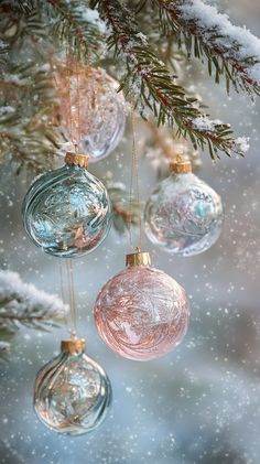 Delicate glass ornaments in soft pastel hues hang from a snowy pine branch, gently swaying. A warm golden light glimmers as snowflakes softly fall in the cozy, softly blurred background. Christmas Tree, Christmas Ornaments, Christmas