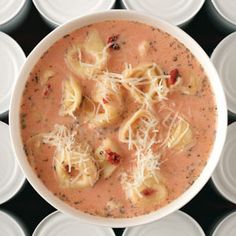 a white bowl filled with pasta and sauce on top of plastic cups next to each other