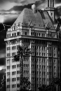 a black and white photo of a building with lightning in the sky behind it on a cloudy day