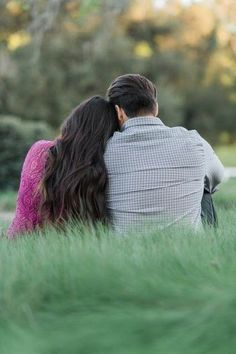 a man and woman sitting in the grass looking at each other with their backs to one another