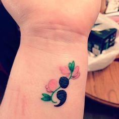 a small tattoo on the wrist of a woman's hand with pink flowers and green leaves