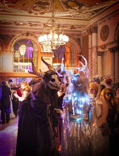 two people in costume standing next to each other near a chandelier with lights on it