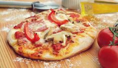 a pizza sitting on top of a wooden cutting board next to tomatoes and pepperoni