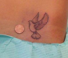 a small bird tattoo on the side of a woman's stomach, next to a penny