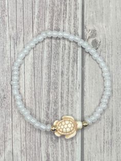 a beaded bracelet with a gold turtle charm on top of white beads and a wooden background