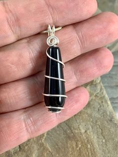 The classic beauty of this long smooth rounded teardrop black onyx necklace is stunning. The deep black color of the stone is beautiful in its simplicity. I chose to enhance this gorgeous gem with a minimalist spiral silver wire design to let the natural beauty shine. Black onyx is an alternate birthstone for July, making this a great gift. *Size 1.5 x .4 inches *Genuine black Onyx Gemstone *Sterling Silver Plated *Includes a Sterling Silver plated chain with a lobster clasp and your choice of l Black Teardrop Pendant For Jewelry Making, Minimalist Black Wire Wrapped Necklace, Black Oval Pendant Minimalist Jewelry, Minimalist Black Teardrop Pendant Necklace, Minimalist Black Oval Pendant Jewelry, Black Onyx Pendant, Wire Wrap Jewelry Designs, Wire Design, Onyx Pendant