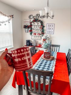 a person holding up a coffee mug in front of a dining room table decorated for christmas